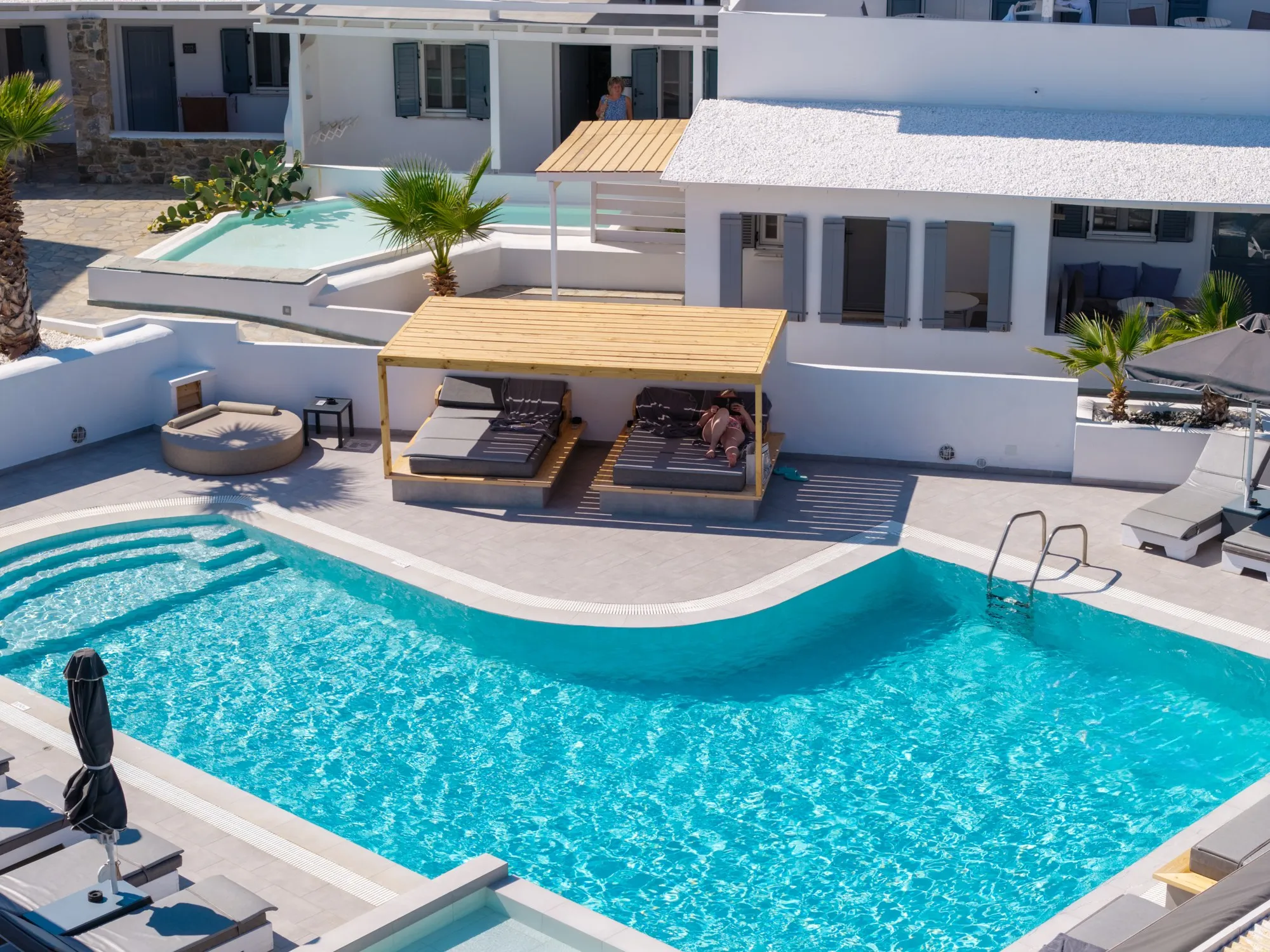 The pool from above, with a pergola over two daybeds and sun loungers along the water